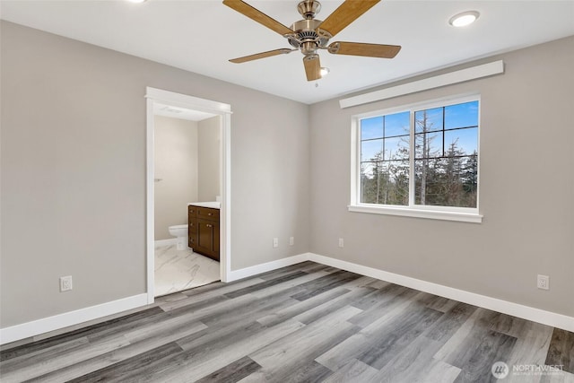 unfurnished bedroom featuring ensuite bath, a ceiling fan, baseboards, and wood finished floors