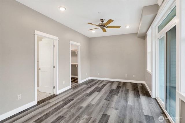 unfurnished bedroom featuring a walk in closet, wood finished floors, recessed lighting, baseboards, and ceiling fan