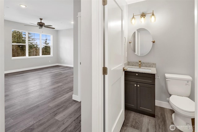 half bath featuring baseboards, ceiling fan, toilet, wood finished floors, and vanity