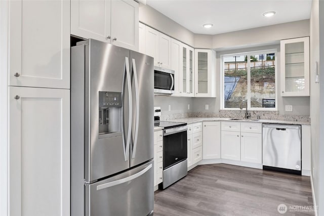 kitchen featuring glass insert cabinets, wood finished floors, white cabinets, stainless steel appliances, and a sink