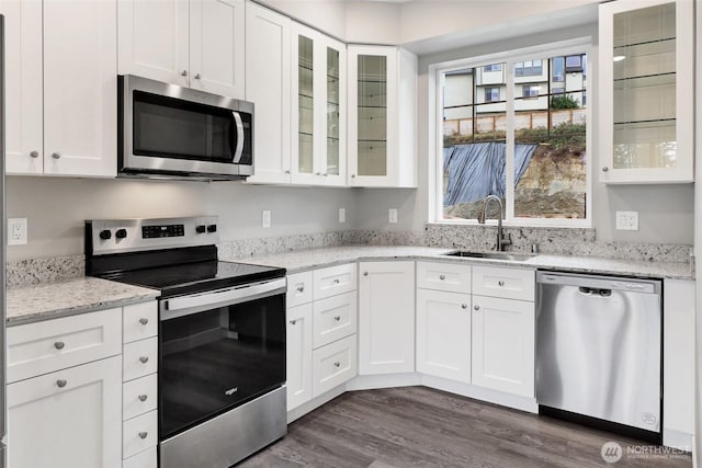 kitchen with light stone counters, dark wood finished floors, a sink, appliances with stainless steel finishes, and white cabinetry