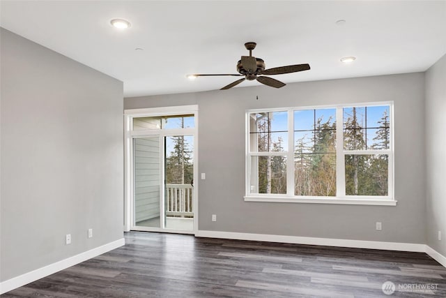 empty room featuring plenty of natural light, baseboards, dark wood-type flooring, and a ceiling fan