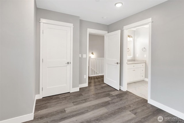 unfurnished bedroom with ensuite bath, baseboards, and wood finished floors