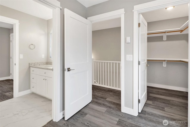 bathroom with vanity, a walk in closet, baseboards, and wood finished floors