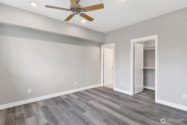 unfurnished bedroom with a walk in closet, wood finished floors, and baseboards