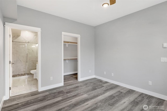 unfurnished bedroom featuring a closet, ensuite bathroom, baseboards, and wood finished floors