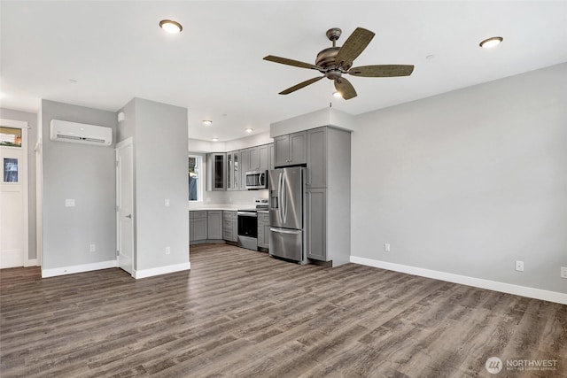 interior space with dark wood finished floors, an AC wall unit, baseboards, and ceiling fan