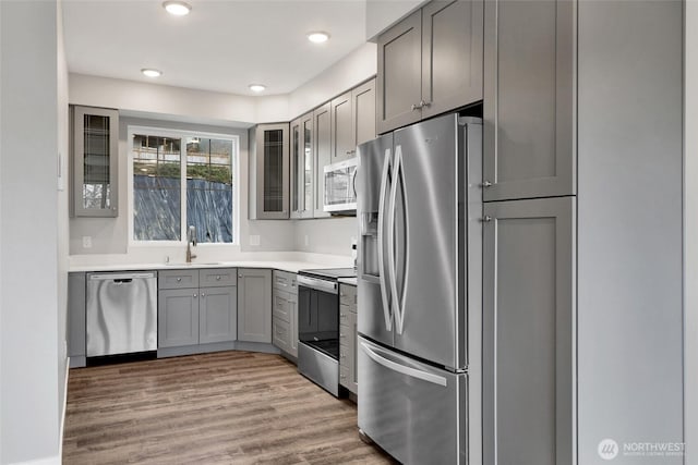 kitchen with glass insert cabinets, gray cabinets, appliances with stainless steel finishes, light wood-style floors, and a sink