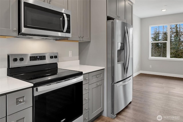 kitchen featuring light wood finished floors, baseboards, light countertops, gray cabinets, and stainless steel appliances