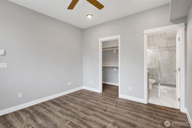 unfurnished bedroom featuring dark wood finished floors, a walk in closet, and baseboards