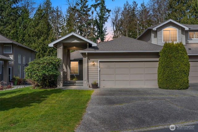 view of front of house featuring aphalt driveway, a yard, an attached garage, and a shingled roof