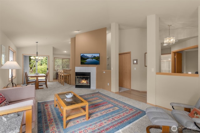 carpeted living area featuring a chandelier, a tile fireplace, and vaulted ceiling