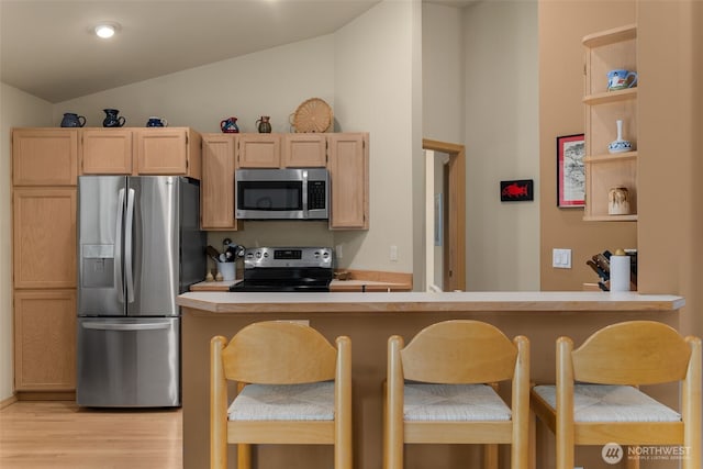 kitchen featuring light brown cabinetry, stainless steel appliances, light wood-style floors, light countertops, and vaulted ceiling