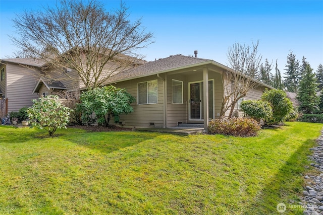 rear view of house featuring a shingled roof, a lawn, and crawl space