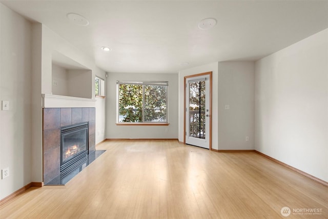 unfurnished living room featuring baseboards, wood finished floors, and a tiled fireplace