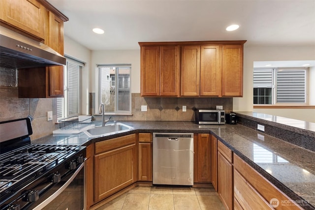 kitchen featuring under cabinet range hood, appliances with stainless steel finishes, brown cabinetry, and a sink