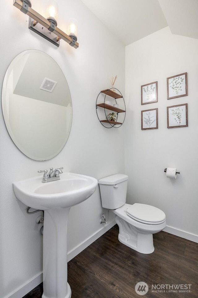 half bath featuring toilet, wood finished floors, visible vents, and baseboards