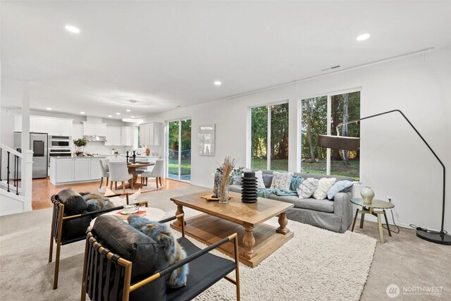 living room featuring stairway, visible vents, baseboards, recessed lighting, and light colored carpet