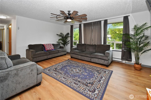 living room with a textured ceiling, wood finished floors, a baseboard heating unit, and ceiling fan