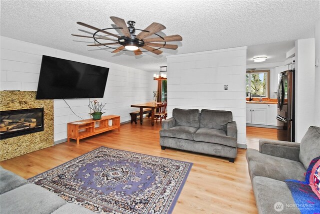 living area featuring ceiling fan with notable chandelier, a textured ceiling, and light wood finished floors