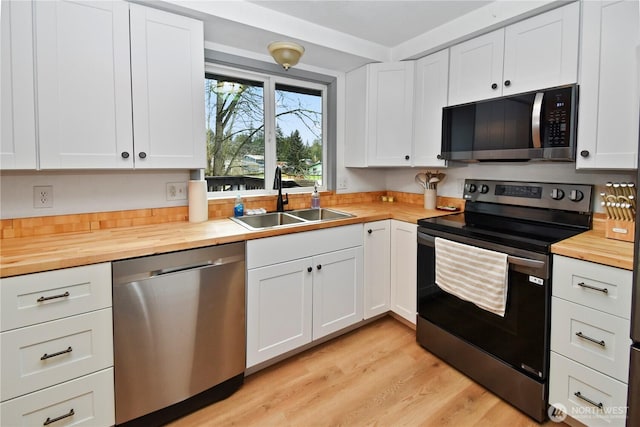 kitchen with butcher block countertops, light wood-style flooring, a sink, white cabinetry, and stainless steel appliances