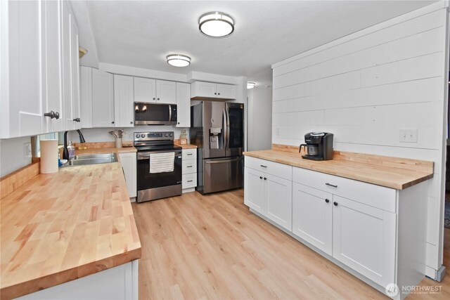 kitchen featuring a sink, white cabinetry, stainless steel appliances, light wood-style floors, and wooden counters