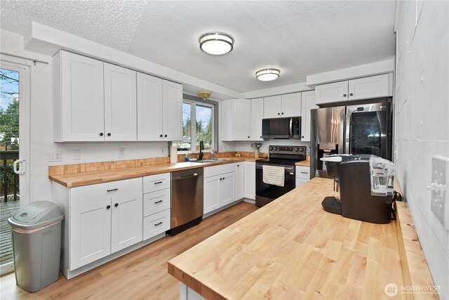 kitchen featuring wooden counters, light wood-type flooring, stainless steel appliances, white cabinetry, and a sink