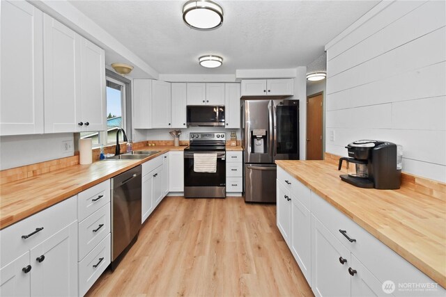 kitchen featuring wooden counters, a sink, white cabinets, appliances with stainless steel finishes, and light wood-type flooring