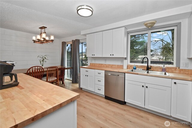 kitchen with light wood-style flooring, a sink, wood counters, stainless steel dishwasher, and white cabinets