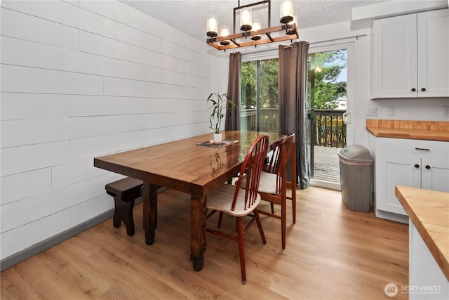 dining space featuring a textured ceiling, an inviting chandelier, light wood-style flooring, and wooden walls