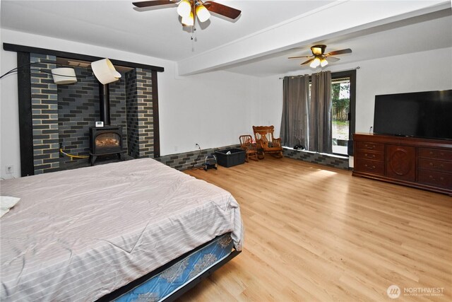 bedroom with beam ceiling, a wood stove, ceiling fan, and wood finished floors