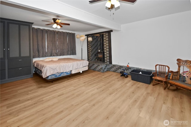 bedroom featuring beam ceiling, a wood stove, a ceiling fan, and wood finished floors