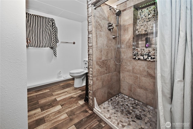 full bathroom with toilet, wood finished floors, and a tile shower