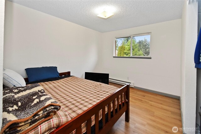 bedroom featuring light wood-style flooring, a textured ceiling, a baseboard heating unit, and baseboards