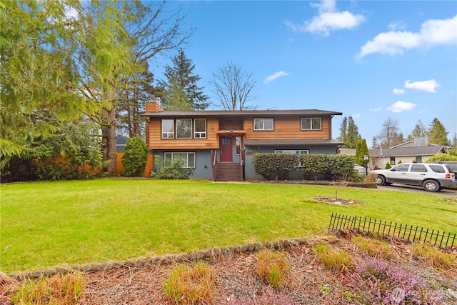 split foyer home featuring a chimney, a front yard, and fence