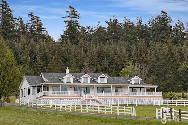 view of front of home featuring a shingled roof, a forest view, a front yard, and fence