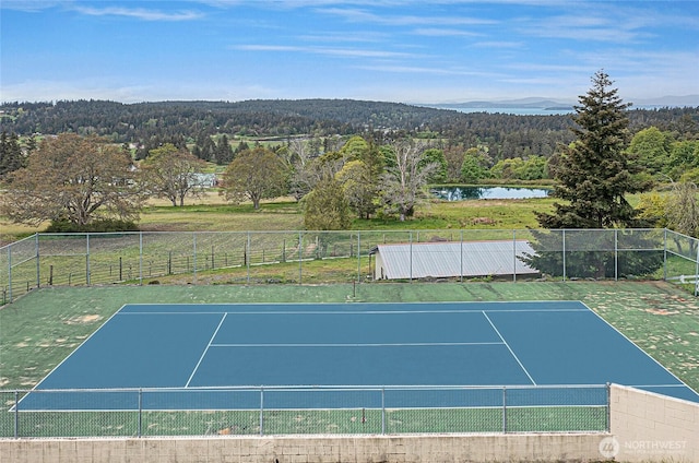 view of sport court featuring a view of trees, fence, and a water view