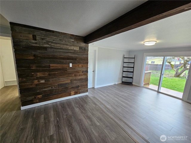 unfurnished living room featuring beam ceiling, a textured ceiling, wooden walls, baseboards, and dark wood-style flooring