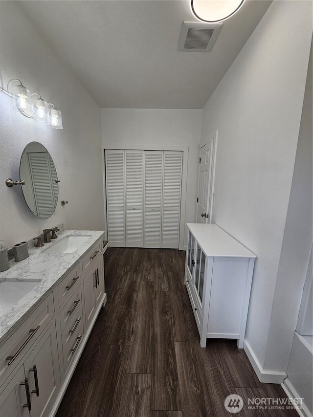 full bathroom featuring visible vents, a sink, wood finished floors, double vanity, and baseboards