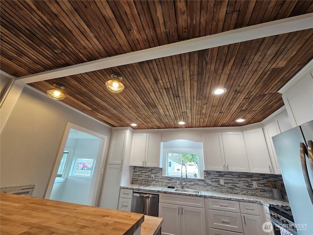 kitchen with butcher block counters, decorative backsplash, appliances with stainless steel finishes, white cabinetry, and a sink