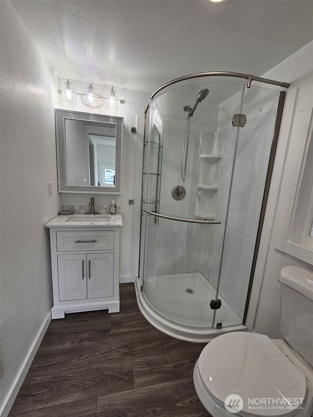 bathroom with toilet, a textured ceiling, wood finished floors, a shower stall, and vanity