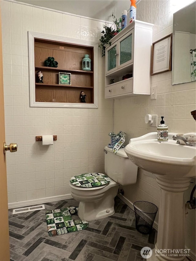 half bathroom featuring tile walls, toilet, and visible vents