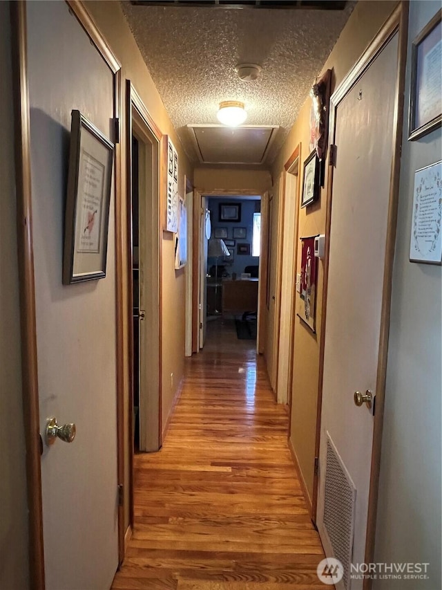 hall featuring light wood-style floors, visible vents, and a textured ceiling