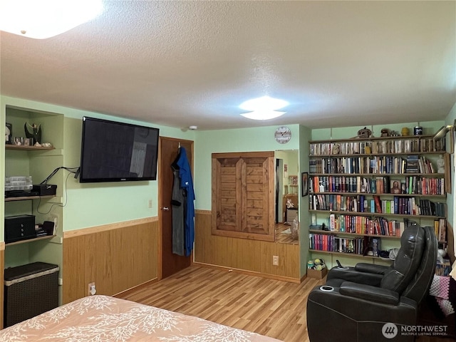 bedroom featuring a wainscoted wall, a textured ceiling, wood finished floors, and wood walls