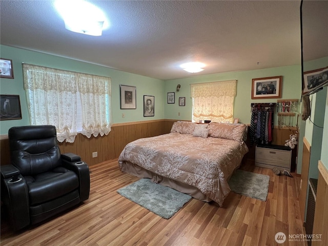 bedroom with wooden walls, wainscoting, a textured ceiling, and wood finished floors