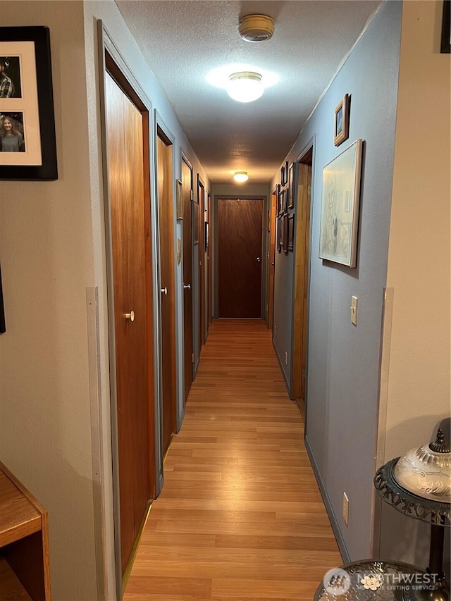 hall with light wood-style flooring and a textured ceiling