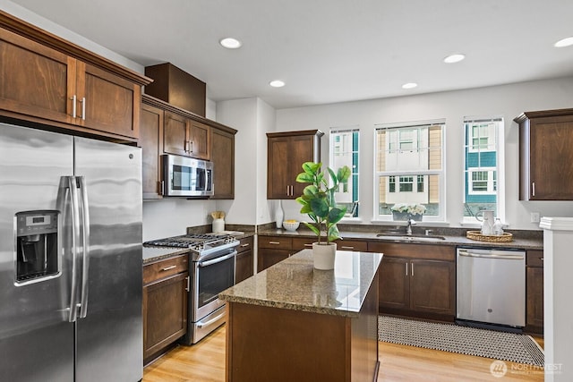 kitchen with a sink, a center island, dark stone counters, light wood-style floors, and appliances with stainless steel finishes