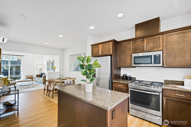 kitchen featuring light wood finished floors, a center island, light stone countertops, recessed lighting, and appliances with stainless steel finishes