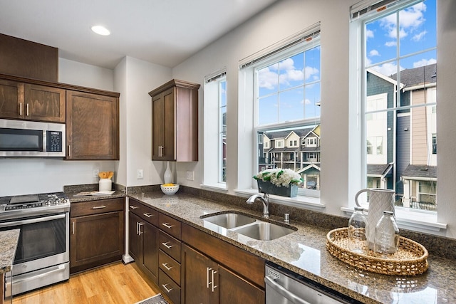 kitchen with light wood finished floors, dark stone counters, a sink, dark brown cabinetry, and appliances with stainless steel finishes