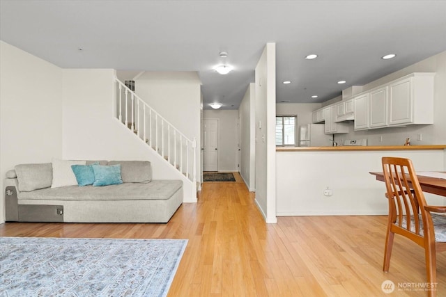 living room with light wood-type flooring, recessed lighting, baseboards, and stairway